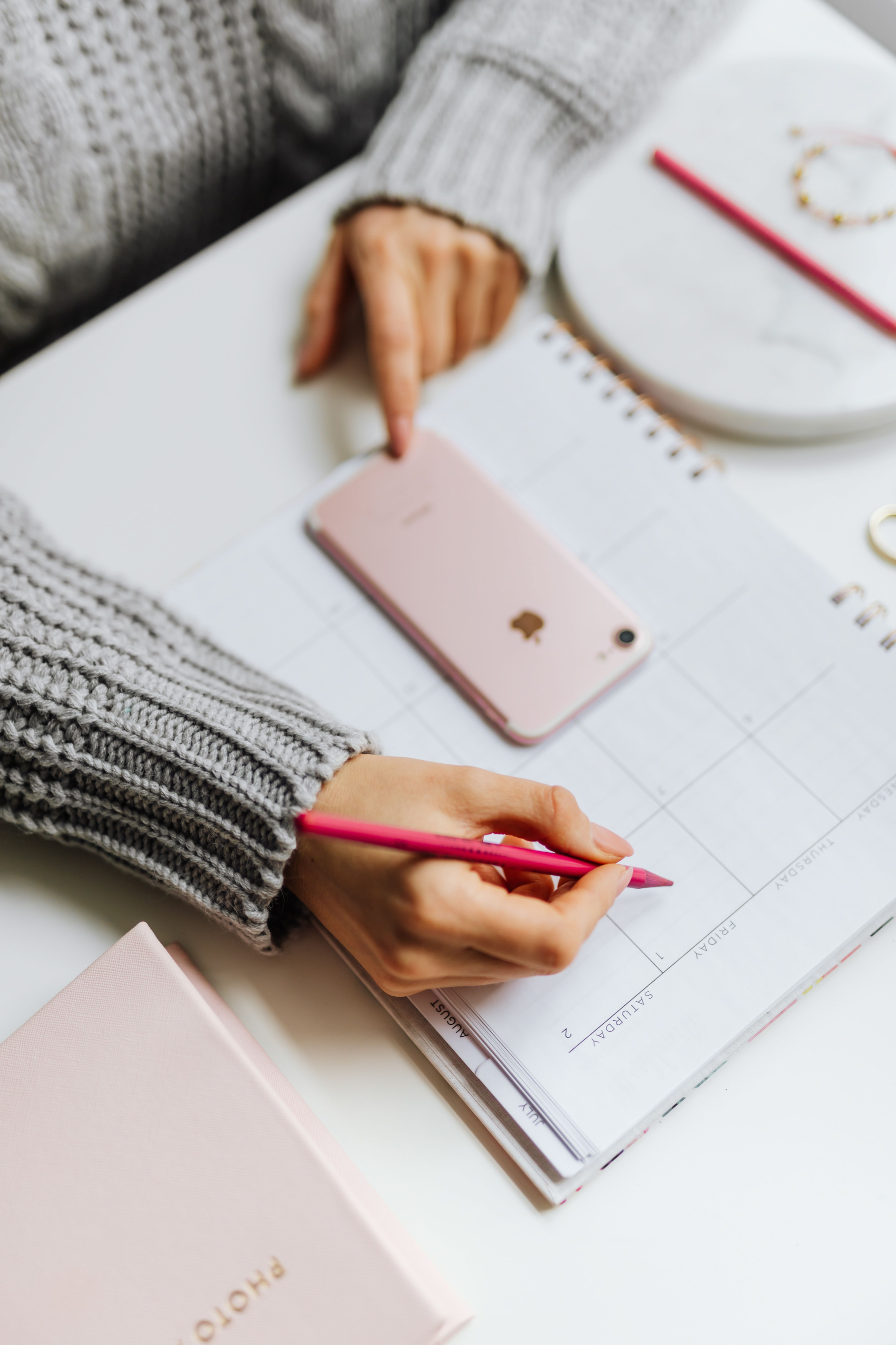 Hände mit Smartphone und Stift über einem Kalender