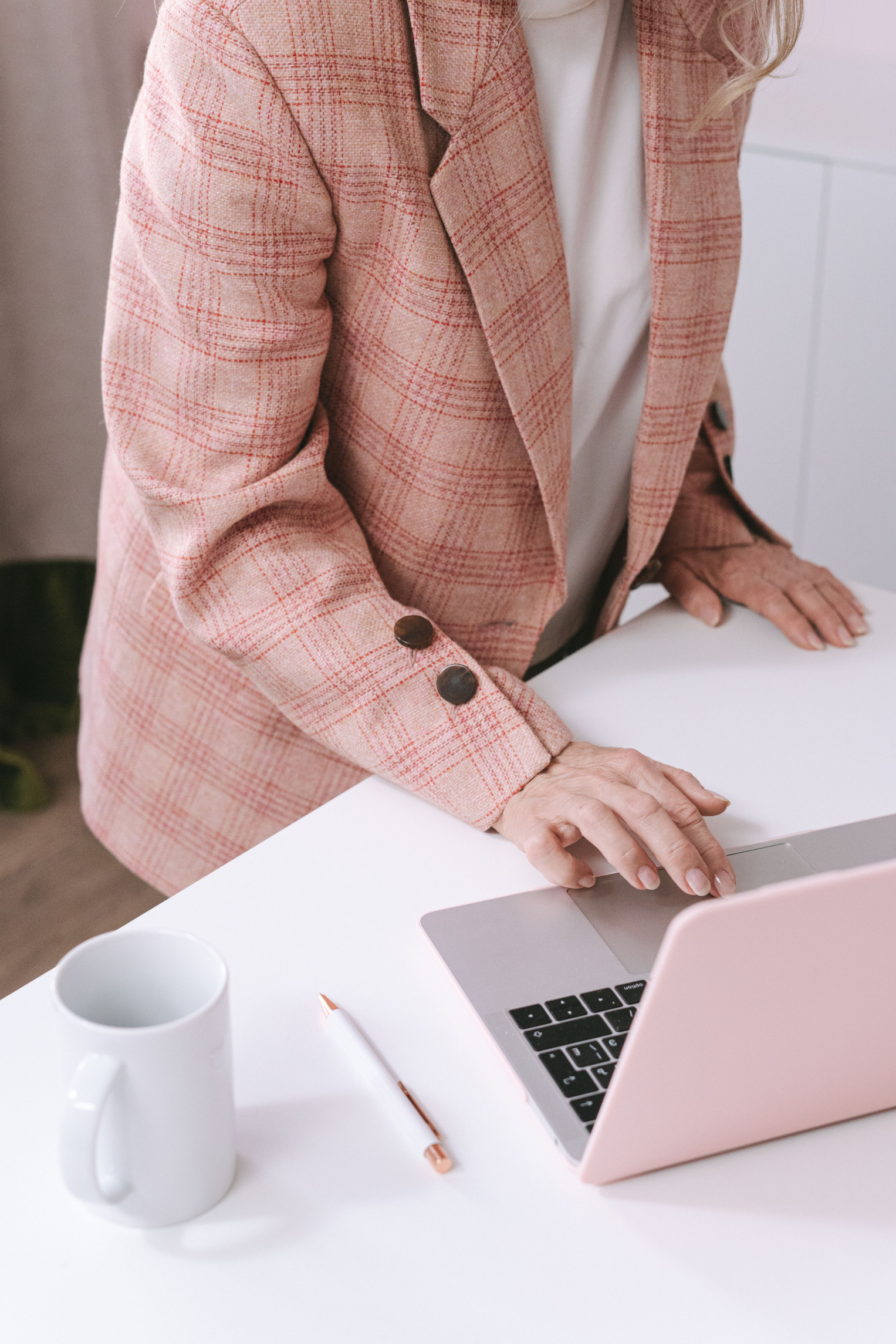 Person im rosafarbenen Blazer arbeitet an einem Laptop